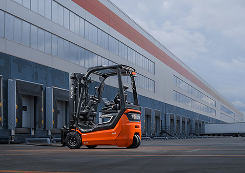 een oranje vorkheftruck van Toyota rijdt van buiten een magazijn binnen